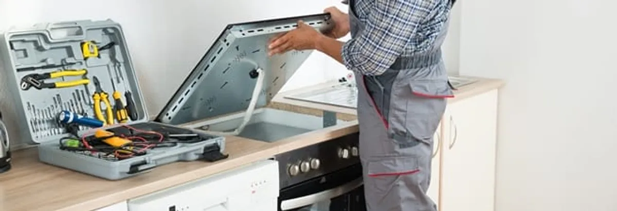 Cooktop repair technician lifting a built-in stovetop for service in Tulsa, OK
