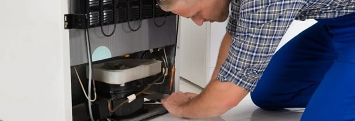Refrigerator repair technician servicing the compressor and condenser area in Tulsa, OK