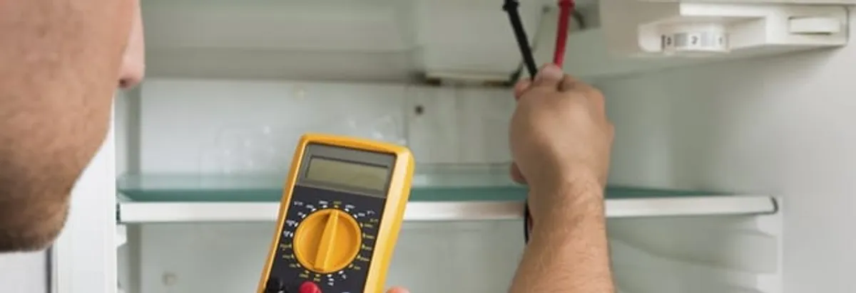 Refrigerator repair technician testing electrical components with a multimeter in Tulsa, OK
